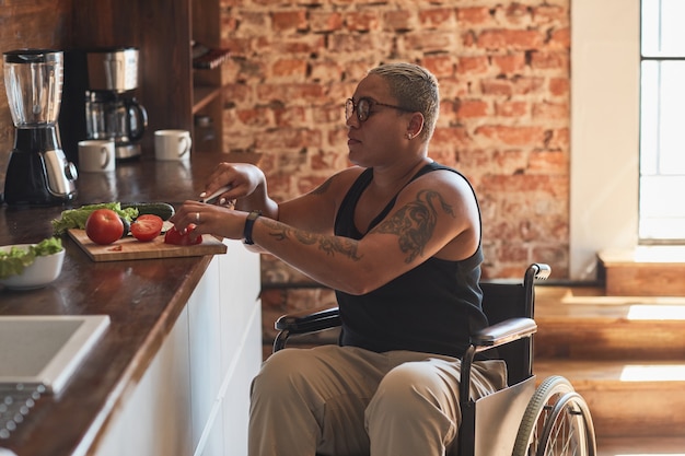 Foto zijaanzichtportret van hedendaagse getatoeëerde vrouw met een handicap die thuis kookt, kopieer ruimte