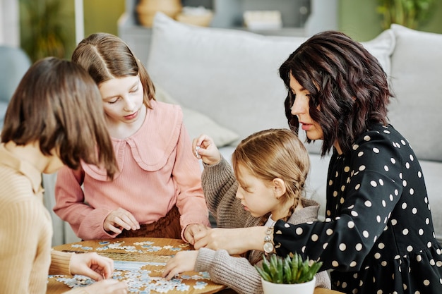 Zijaanzichtportret van jonge moeder met drie kinderen die samen met puzzel spelen in de thuisomgeving