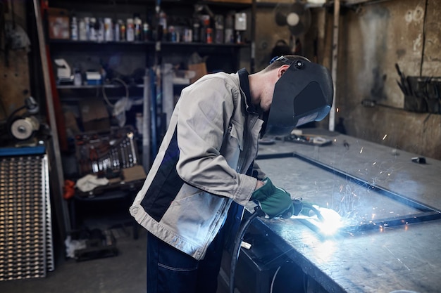 Zijaanzichtportret van mannelijke arbeider die metaal in industriële fabrieksworkshop lassen met nadruk op vonken