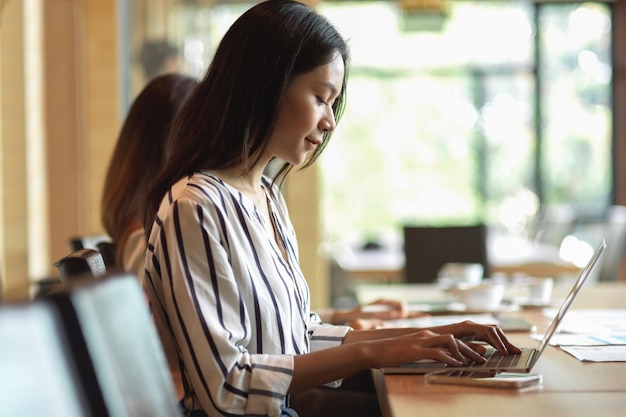 Zijaanzichtportret van zakenvrouw die blij is met haar werk met generieke laptop op kantoor, wazige achtergrond