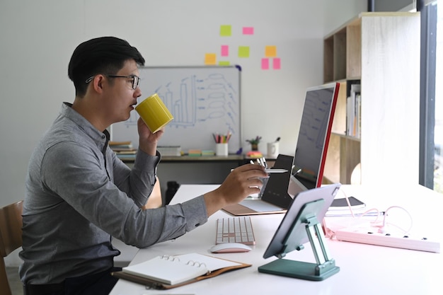 Zijaanzichtzakenman die koffie drinkt en aandelenmarkt analyseert op desktopcomputer