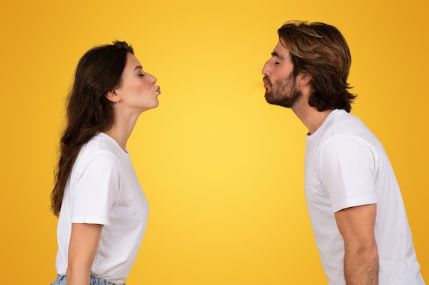 Zijdeprofiel van een jonge man en vrouw in witte T-shirts die tegenover elkaar staan met gerimpelde lippen