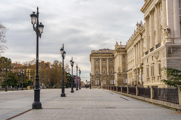 Zijgevel van het koninklijk paleis van madrid, voetgangersstraat met lantaarnpalen, bomen en zonnige dag met wolken. spanje.