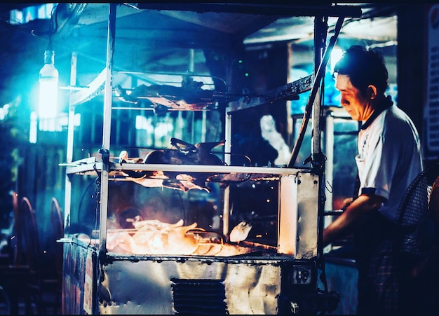 Foto zijkant van chef-kok die vlees grillt bij een eetkraam