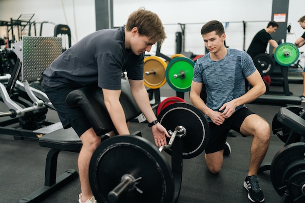 Foto zijkant van de trainer die een beginnende sporter helpt om correct scott curls te doen met barbelllifting