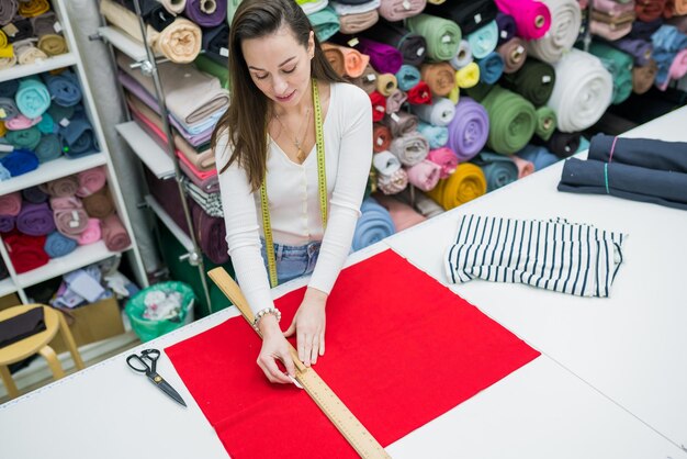 Foto zijkant van een brunette vrouw die stof meet op een werktafel in een textielwinkel