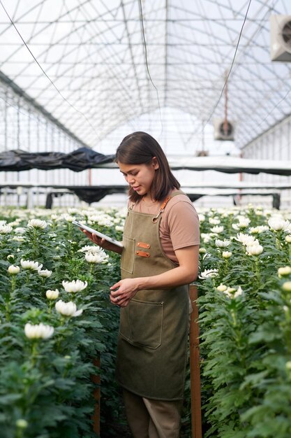 Zijkant van een jonge brunette vrouwelijke bloemist die in het gangpad tussen bloembedden staat