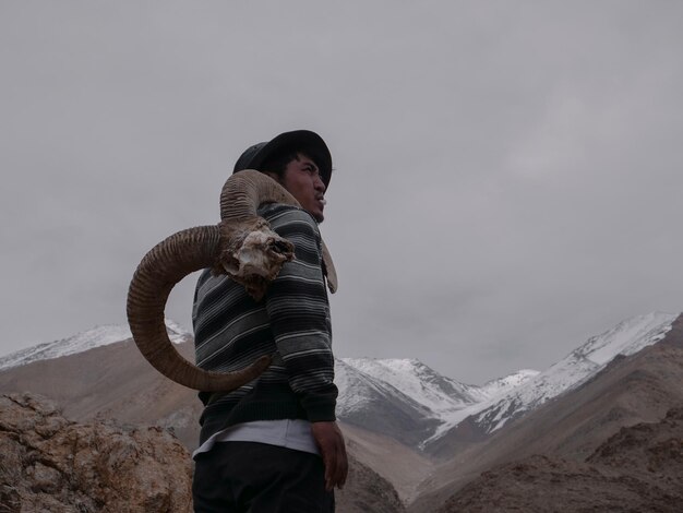 Foto zijkant van een jonge man met hoorns terwijl hij op de berg staat tegen een bewolkte hemel