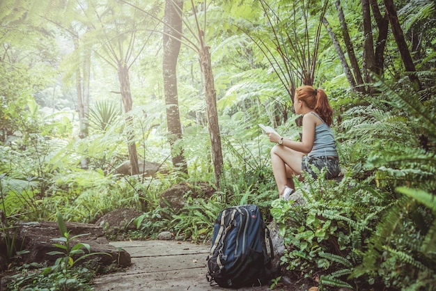 Foto zijkant van een jonge vrouw met een boek die in het bos zit