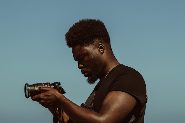Zijkant van een man die met een camera fotografeert tegen een heldere blauwe lucht