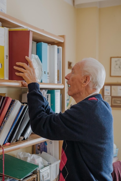 Foto zijkant van een oudere man die een boek op een plank houdt