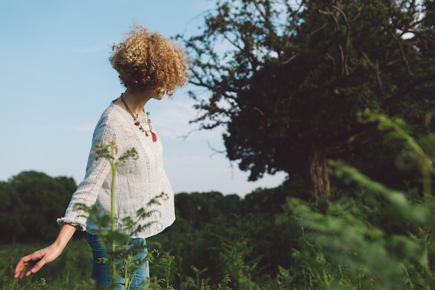 Zijkant van een volwassen vrouw die bij bomen en planten op het veld staat