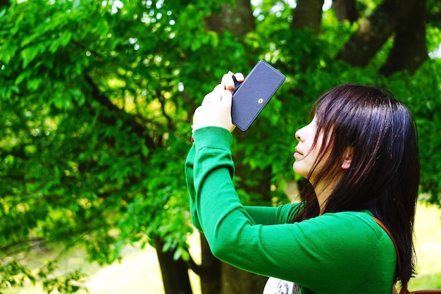 Foto zijkant van een vrouw die bomen in een park fotografeert