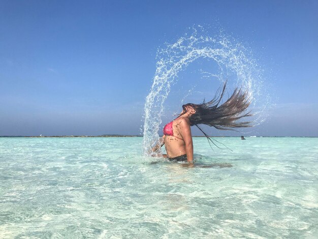 Foto zijkant van een vrouw die haar gooit terwijl ze in de zee staat tegen een heldere lucht