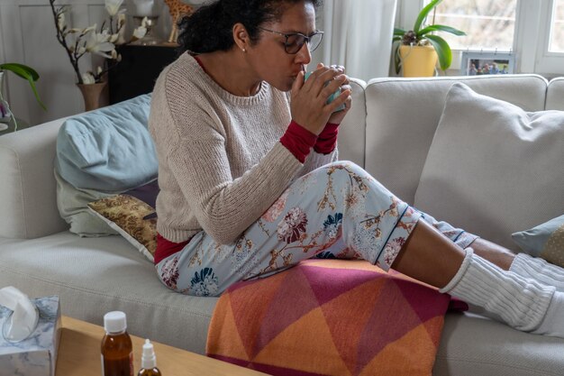 Foto zijkant van een vrouw die koffie drinkt terwijl ze thuis op de bank zit