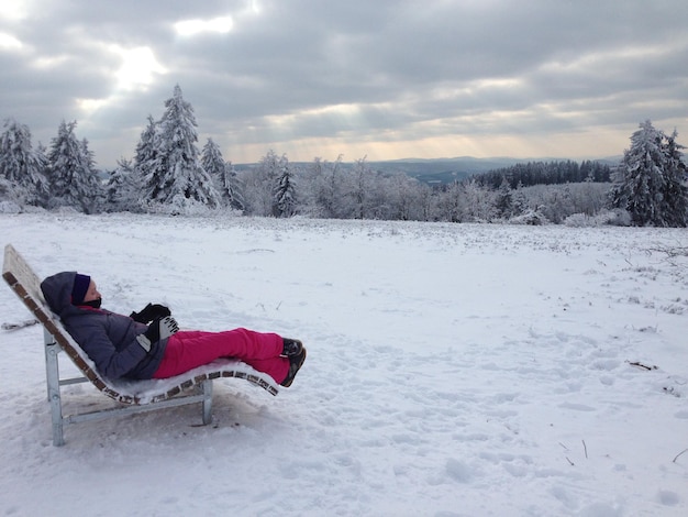 Foto zijkant van een vrouw die ontspant op een ligstoel over een met sneeuw bedekt veld