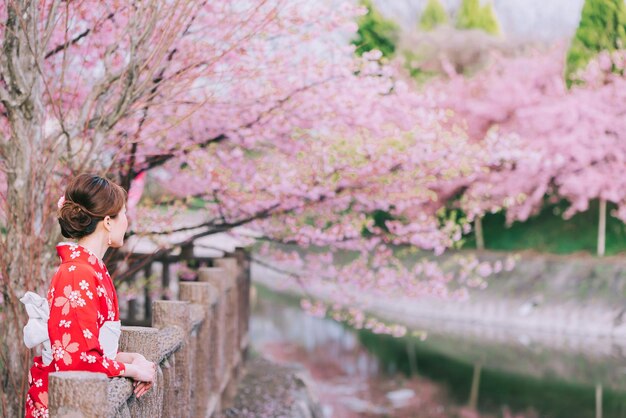 Foto zijkant van een vrouw die tegen roze kersenbloesembomen staat
