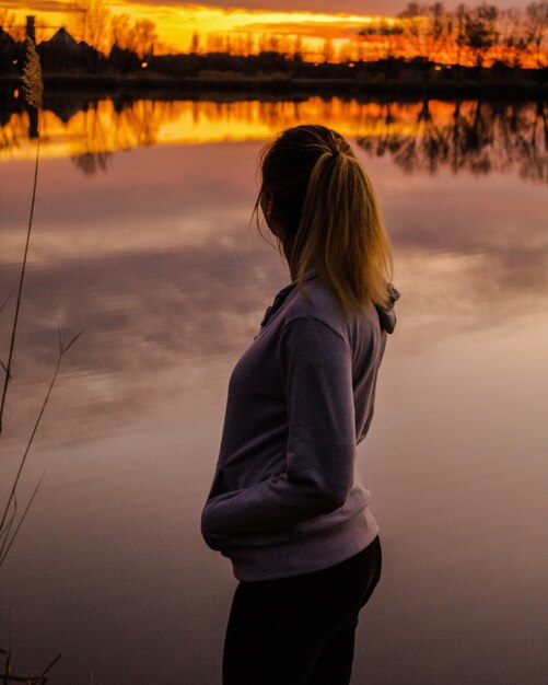 Foto zijkant van een vrouw die tijdens de zonsondergang naar het meer kijkt tegen de lucht