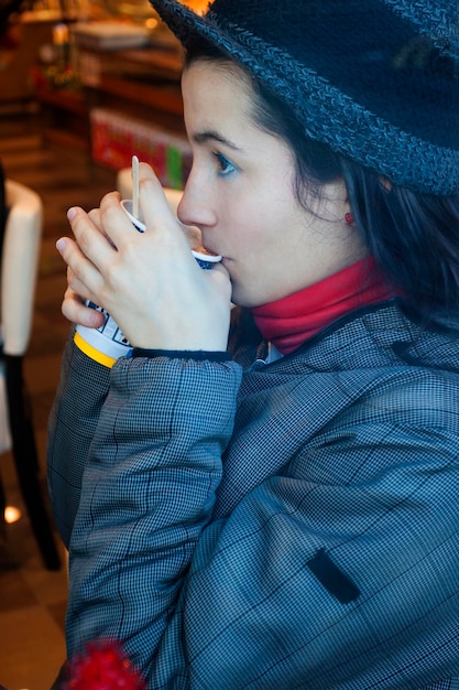 Foto zijkant van een vrouw die warme kleding draagt terwijl ze koffie drinkt in een café