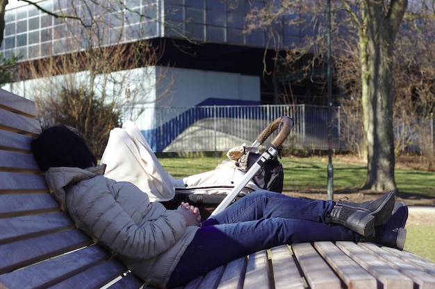Foto zijkant van een vrouw die zich op een bankje ontspant met een kinderwagen in het park
