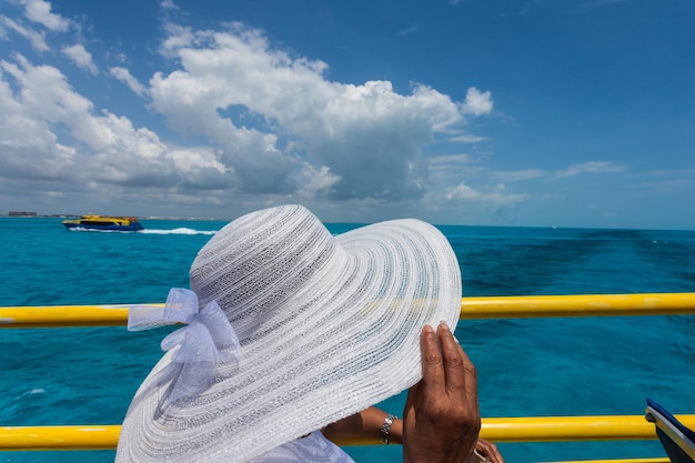 Foto zijkant van een vrouw met een hoed terwijl ze bij een reling tegen de zee staat