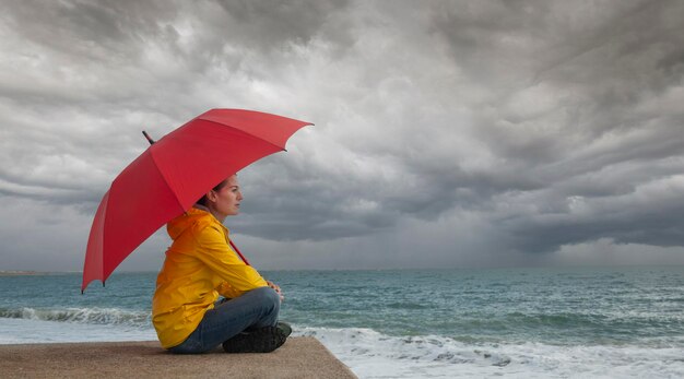 Foto zijkant van een vrouw met een rode paraplu op het strand tegen de lucht