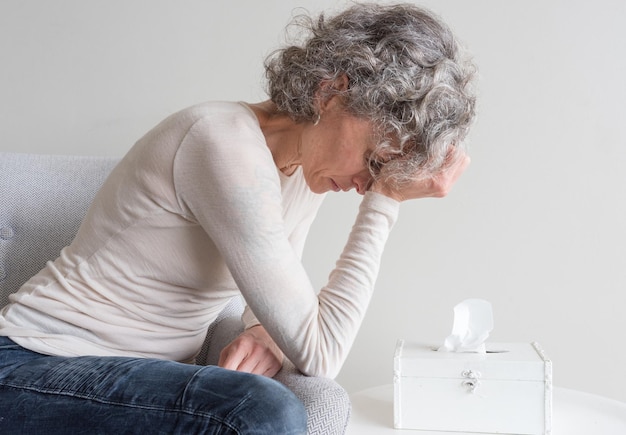 Foto zijkant van gestresseerde volwassen vrouw met hoofd in hand die thuis tegen de muur zit