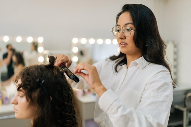 Zijkant van haarstylist die golven maakt die op vrouwelijk haar krullen Closeup van vrouwelijke haarstijlist in een schoonheidssalon neemt een haarlok en drukt met een haarregelaar