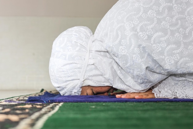Zijkant van religieuze Aziatische moslimvrouw die tot God bidt in Sujud-houding op een gebedsmat