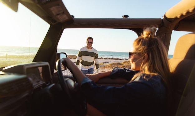 Zijkantbeeld van een blank echtpaar, de vrouw in een open auto met het stuur in handen, de man die naar zijn partner kijkt