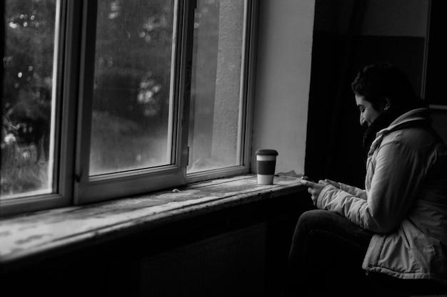 Foto zijkantbeeld van een glimlachende vrouw die thuis bij het raam een telefoon gebruikt