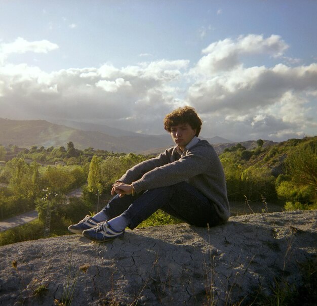 Foto zijkantbeeld van een jonge man die op een berg tegen de lucht zit