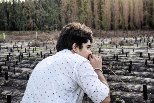 Foto zijkantbeeld van een jonge man die wegkijkt terwijl hij op het veld tegen bomen kruipt