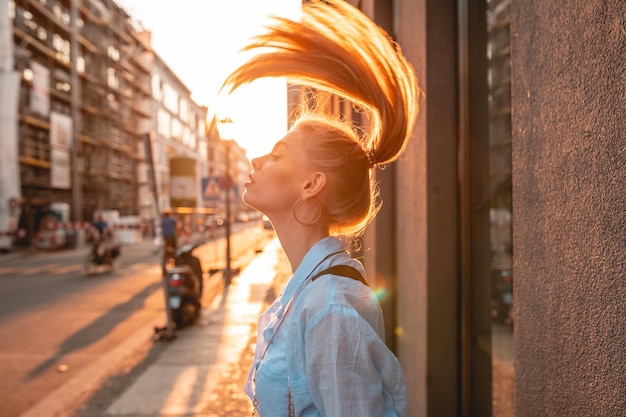 Zijkantbeeld van een jonge vrouw die haar gooit terwijl ze tijdens de zonsondergang op het trottoir staat