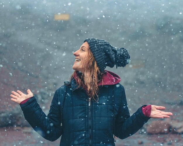 Foto zijkantbeeld van een jonge vrouw met uitgestrekte armen die buiten staat met een lepel sneeuw die valt