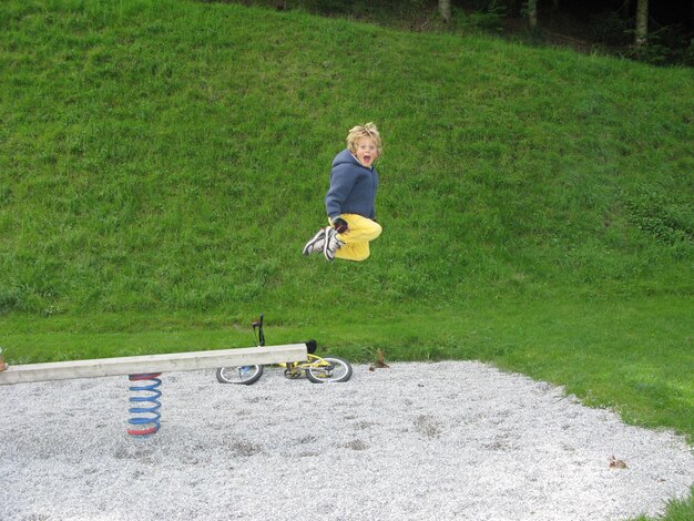 Foto zijkantbeeld van een jongen die schreeuwt terwijl hij van een lentejacht in het park springt