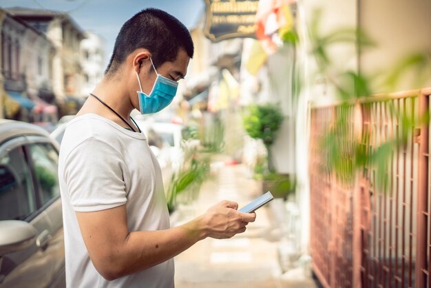 Zijkantbeeld van een man die een masker draagt en een mobiele telefoon gebruikt terwijl hij buiten staat
