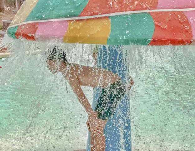 Foto zijkantbeeld van een shirtloze jongen die onder de douche bij het zwembad staat