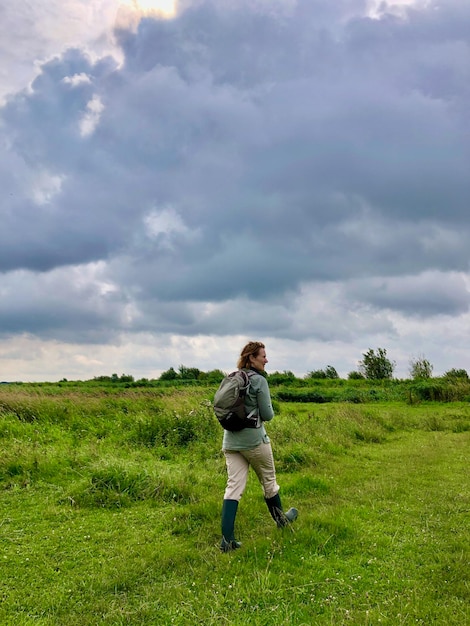 Foto zijkantbeeld van een vrouw die onder een indrukwekkende wolk over een groen veld wandelt