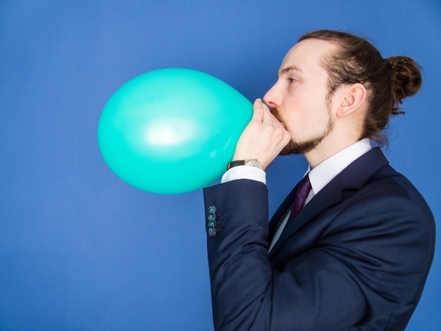 Foto zijkantbeeld van een zakenman die een groene ballon blaast op een blauwe achtergrond