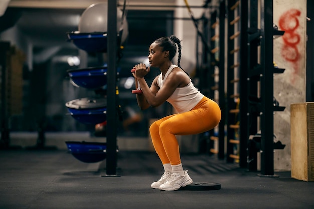 Foto zijkantbeeld van een zwarte sterke sportvrouw die met gewichten oefent in een squatpositie