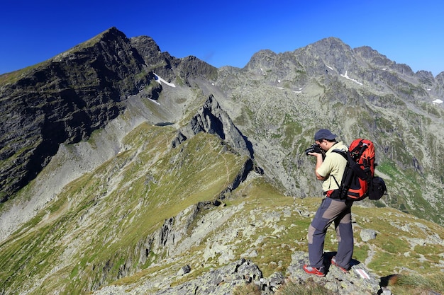 Zijkantbeeld van rugzakman die door middel van een camera op de top van de berg fotografeert