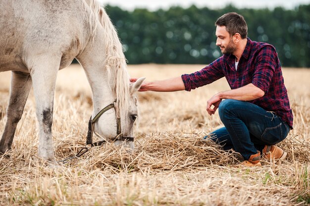 Zijn beste vriend. Zijaanzicht van jonge boer die paard aanraakt terwijl hij buiten zit