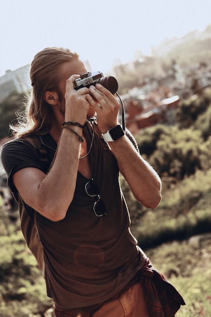 Zijn passie. Jonge man in vrijetijdskleding die het uitzicht fotografeert