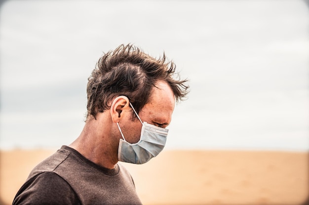 Zijportret jonge man draagt beschermend masker gezichtsuitdrukking emotie kijk naar beneden duin Concept COVID-stresssyndroom geestelijke gezondheid angst voor gevaar besmetting nadelige sociaaleconomische gevolgen