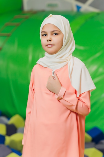 Foto zijportret van een klein moslimmeisje dat een hijab draagt. concept van moslimkleding voor kinderen. tegen de achtergrond van de speeltuin.