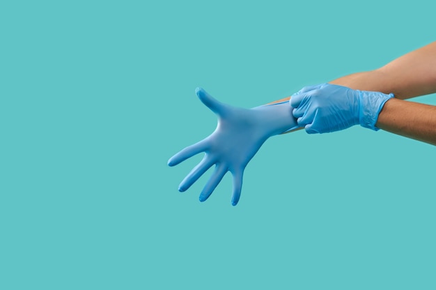Zijportret van onherkenbare persoonshanden die blauwe medische beschermende steriele latexhandschoenen dragen die op een blauwe achtergrond worden geïsoleerd