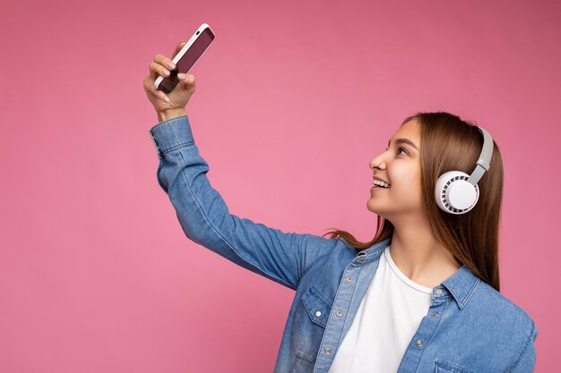 Zijprofielfoto van aantrekkelijke positieve glimlachende jonge donkerblonde vrouw die modieuze blauwe jeans draagt