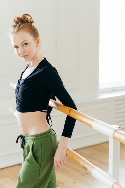 Zijwaarts schot van aantrekkelijke slanke danseres staat terug naar ballet barre rekt lichaam uit voordat training zwarte top draagt en joggingbroek heeft een fit lichaam woont kunstacademie repetities binnen bij