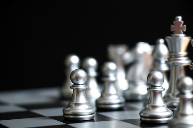 Zilveren pion is aan de eerste zet in schaakspel op zwarte achtergrond (Concept voor zakelijke beslissing, start of begin project)